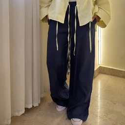 - What it is: A pair of dark navy wide-leg pants with a relaxed, flowy fit.
- Intended audience: Unisex or potentially women’s, judged from the loose silhouette and styling with a cropped top and long drawstring details.
- Visible attributes: Deep navy fabric, high waist with long white drawstrings, wide leg / palazzo style, light-colored top partially tucked, white sneakers. No visible branding.