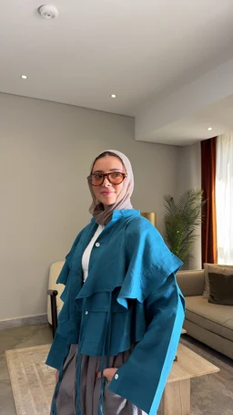 - What the product is: A layered shirt or jacket in a bold midnight blue shade, shown as a loose, draped outer layer with wide, cape-like sleeves and an attached belt detail over a lighter inner layer.
- Apparent intended audience: Women, based on styling, hijab-friendly look, and fitted underlayer; designed for a modest, contemporary fashion audience.
- Notable attributes visible: Midnight blue color with a lighter inner top, oversized, flowing silhouette, layered cape-like outer panel, long sleeves, button-front opening, and a relaxed, draped fit. Material appears lightweight and smooth, with a slightly structured drape.