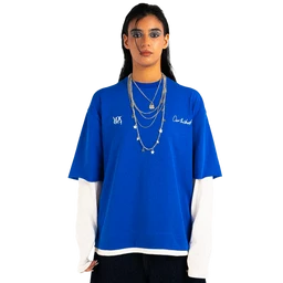 - What it is: A blue short-sleeve T-shirt layered over a white long-sleeve shirt, styled with multiple silver chains.
- Intended audience: Unisex look suitable for men’s or women’s fashion, inferred from the oversized, relaxed fit and layering.
- Notable attributes: Bright royal blue body with white long sleeves underneath, additional white trim at hem, and layered silver chain necklaces as styling. The fabric appears to be a knit cotton blend with a casual, streetwear vibe.