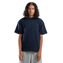 This is a navy basic short-sleeve t-shirt with a relaxed fit, worn by a male-presenting model. The shirt appears solid navy with a small, subtle logo on the left chest and a standard crew neckline, paired with light gray bottoms for contrast. Notable attributes visible: cotton-like fabric, midweight knit, and a clean, minimal styling suitable for casual wear.