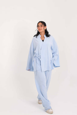 - Product: A matching loungewear set in baby blue consisting of a wrap-style top and wide-leg pants.
- Intended audience: Women (styled on a female model with relaxed, cozy-fit silhouette).
- Notable attributes: Light pastel blue color, soft, fluid fabric, wrap/obs wrap tie detail at the waist, long sleeves with wide cuffs, relaxed drape, full-length pants, casual/comfort wear look.