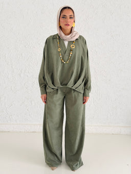 - Description: A loose olive-green matching set with a long-sleeve top and wide-leg pants. The top has a relaxed fit with a knotted front detail, and the pants are high-waisted with a wide leg and cuffed hems. The model wears a light-colored headscarf and layered necklace, giving a modest, boho styling.

- Audience and styling cues: Appears targeted toward women, with a modest-cut silhouette and relaxed, comfortable fit suitable for casual or semi-formal wear.

- Notable materials and colors: Olive-green fabric with a soft, textured look; gold-toned necklace accessories enhance the ensemble. The overall style is relaxed, bohemian-inspired lounge-casual.