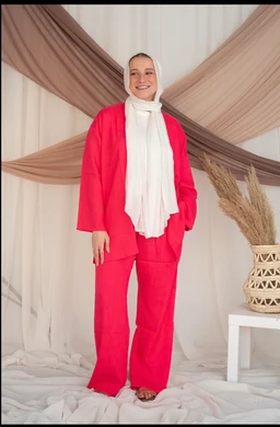 - Product: Watermelon amary linen pants set (visible as a matching jacket and wide-leg pants).
- Audience: Women (model styling with modest hijab and feminine fit suggests womenswear).
- Notable attributes: Bright watermelon pink color, linen fabric texture, relaxed wide-leg trousers with a matching blazer, white headscarf/inner top. Styling is bold, monochrome with a contrasting white scarf.