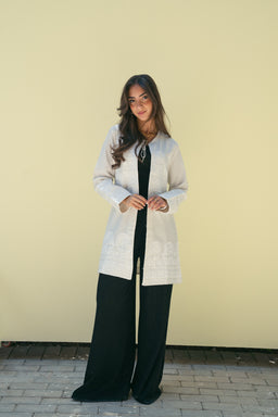 - A women’s long-sleeve cardigan or open-front knit layer in ivory, worn over a black top and wide-leg black trousers. The model presents a sophisticated, minimalist look with a knit texture and a knee-length cardigan style.
- Intended audience: women.
- Notable attributes: ivory/cream color, knit fabric, longline cardigan style with a subtle pattern; black wide-leg pants worn underneath; overall elegant, soft, and versatile outfit suitable for a smart-casual look.