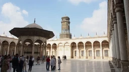 - What the product is: A travel tour image showcasing a courtyard in Cairo with arches, a central pavilion, and a tall tower in the background.
- Intended audience: Unisex audience (photo centers on travel experience; no gender-specific styling).
- Notable attributes: Light-colored stone architecture, open-air courtyard, arched colonnades, domed canopy structure, bright daytime sky; casual, everyday clothing on people. The scene conveys a cultural or sightseeing tour experience.