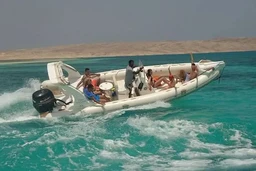 - What the product is: A high-speed motorboat (inflatable/rigid-hull) with a crew on board, speeding across turquoise coastal water.
- Intended audience: Unisex or general recreational boating fans; scenes suggest leisure and island/holiday use.
- Notable attributes visible: White boat with multiple passengers, outboard motor (black) at the stern, clear blue-green sea, small island or sandy shoreline in the background, open deck with seating and steering console, daytime sunny weather. Material/style cues imply a rugged, inflatable or rigid-hull boat designed for fast inland/offshore transport.