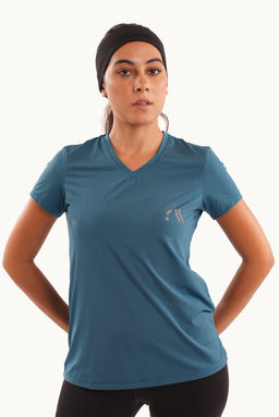 The image shows a short-sleeve athletic T-shirt in a blue-teal color with a V-neck. The model appears to be a woman, styled for active wear, wearing a black headband and black leggings, suggesting a women’s audience. Notable visible features include moisture-wicking fabric with a subtle sheen, a small light-colored logo on the left chest, and a relaxed yet athletic fit with minor sleeve shaping. The overall style is sporty, suitable for workouts or casual athletic wear.