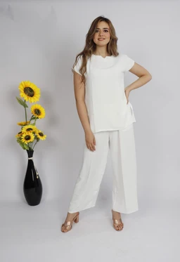- What the product is: A white two-piece lounge/pareo-style set consisting of a short-sleeve top and wide-leg cropped pants, styled for a relaxed, casual look.
- Intended audience: Women's or unisex (based on model and styling).
- Notable attributes: Crisp white fabric, short sleeve top with a loose fit and side tie element, wide-leg cropped pants, soft drape, lightweight material; simple, minimalist styling with nude sandals; background features a vase with sunflowers.