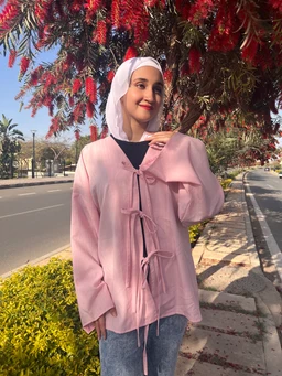 - Product: Pink Powder tie top worn as a loose outer layer, styled over a dark inner top.
- Audience: Women (adult) inferred from the feminine styling, hijab and soft pastel color.
- Notable attributes: Light pink powder shade, oversized relaxed fit, long sleeves, tie-front closures, soft textured fabric, light, casual-layered look.