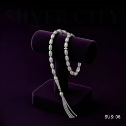 - A silver prayer bead string (rosary) with oval 33 beads, length around 24 cm, featuring a long longitudinal engraving area and a tassel. 
- Target audience appears unisex (modeling suggests general wear, suitable for both men and women). 
- Visible materials and style: solid silver (925) beads with a polished, shiny finish; oval-shaped beads arranged in a continuous strand, ending in a decorative multi-strand tassel; presented on a dark purple display stand to highlight the jewelry.