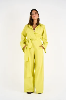The image shows a lime-yellow two-piece set consisting of a long-sleeve shirt with a V-neck and wide-leg high-waisted pants, tied at the waist with a matching belt. It appears designed for adults, likely women, based on the model and styling (plunging neckline, flared sleeves, and billowy silhouette). Notable attributes include the bright lime color, lightweight-looking fabric, wide-leg cut, and a waist-tie belt for a cinched waist.