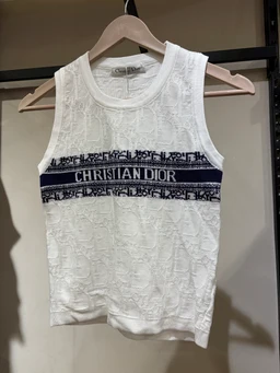 - What it is: A sleeveless knit tank top with a rounded neckline, shown on a hanger.
- Intended audience: Women (based on feminine fit and styling).
- Notable attributes: White knit fabric with a navy patterned horizontal band across the chest featuring the text “CHRISTIAN DIOR.” The garment has a sleeveless design, ribbed crew neckline, and a slightly cropped length. The pattern appears as a repeat motif within the band, contributing a luxury “brand-inspired” look without naming beyond the visible text.