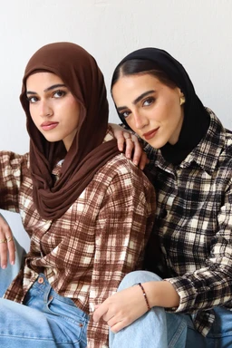 - What the product is: A layered plaid shirt/jacket set styled as a coordinated two-piece look, shown on two women wearing hijabs.
- Apparent audience: Women (unisex styling but modeled by female-presenting individuals; intended for women's wear).
- Notable attributes: Plaid fabric in earthy brown and cream tones on one model and black-and-white plaid on the other; button-front shirt with a relaxed, oversized fit; layered styling with headscarves (hijabs) and light blue jeans; casual, everyday fashion vibe. Material appears to be woven/flannel-like with a soft, textured surface. Color palette includes brown, cream, black, and white. Style is casual, outdoor/cozy layered plaid.