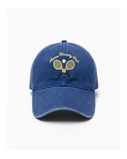 A washed blue baseball cap with a curved brim. It’s styled for a unisex or casual outdoor look, with embroidered yellow text and crossed tennis rackets on the front. Visible details include the washed navy fabric, six-panel construction, and a small button top.