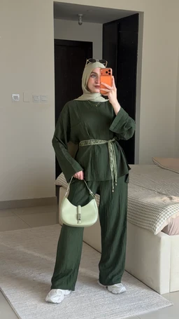 - What the product is: A matching olive green two-piece set consisting of a loose, long-sleeve top with a wide, belted waist and wide-leg pants. The belt and the functional pockets add definition to the outfit.
- Apparent audience: Women (modest styling with a hijab and layered look suggests adult female fashion).
- Notable attributes: Olive green color; soft, relaxed-fit fabric; long sleeves; wide-leg pants; matching belt; belt loops; hijab in a light beige/cream tone; white sneakers and a light-colored handbag as accessories in the photo. The overall style is modest, casual-chic with a coordinated set.