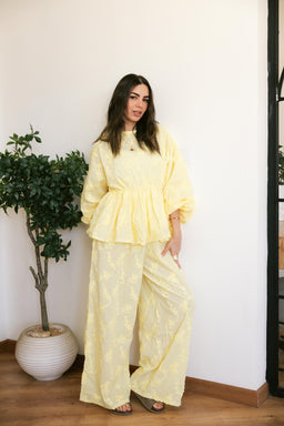 - This is a women's fashion set in pale yellow. The model is wearing a matching peplum-top and wide-leg pants in a light, textured floral or damask-like pattern, with soft, voluminous sleeves for the top and a relaxed silhouette for the pants.
- Notable details: breathable, lightweight fabric in a pale yellow shade; peplum waist creates a flattering cinch; oversized puff sleeves; wide-leg pants for a comfortable, flowy look. The styling is casual yet dressy, suitable for warm weather or relaxed events. The photo emphasizes a cohesive two-piece set with a delicate, summeryPrint.