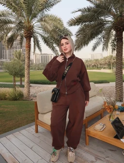 - What the product is: A matching brown loungewear set (hoodie-style top and loose jogger pants) in a modal fabric.
- Apparent audience: Unisex-leaning women’s/Men’s casual streetwear, styled on a female model.
- Notable attributes visible: Solid chocolate brown color, relaxed oversized hoodie with dropped shoulders, elastic waist joggers, light beige sneakers, small black crossbody bag, hijab coordinating with the outfit. Fabric appears soft and drapey (modal), with a casual, comfortable, athleisure vibe.