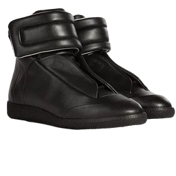 These are black leather high-top sneakers with a padded Velcro strap closure across the ankle for a secure fit. The design reads as unisex with a minimalist, sporty silhouette and a matte leather finish. Notable details include the thick cushioned ankle strap, rounded toe, and a flat rubber sole.