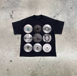 - What it is: A black short-sleeve T-shirt featuring a grid of nine circular metallic graphic discs printed on the front.
- Intended audience: Unisex/suitable for men or women based on styling; the oversized, boxy fit and simple crew neckline suggest a unisex streetwear look.
- Notable attributes: Visible metallic-looking discs with varying patterns and textures arranged in a 3x3 grid; monochrome silver-gray tones on a black T-shirt; casual crew neck, standard short sleeves. No branding or logos visible.