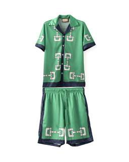 - Product: A two-piece set consisting of a short-sleeve polo shirt and matching shorts.
- Intended audience: Unisex look, but styling and sizing appear suitable for men's or boys' wear.
- Notable attributes: Bright green fabric with dark navy trim and a repeated white chain-link pattern. The shirt features a button-front placket and a spread collar; shorts have an elastic waistband and side panels in navy with the same anchor-like pattern. The material appears lightweight and shiny, suggesting a satin-like or synthetic finish.
