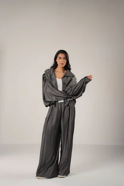 A women's loungewear set made from Tencel with a draped, oversized jacket and wide-leg pants. The look is relaxed and contemporary, styled with a white inner top, and the fabric appears soft, drapey, and silky in a dark charcoal/gray shade. Notable attributes: shimmering, fluid texture, tonal monochrome, and a coordinated two-piece casual couture vibe.