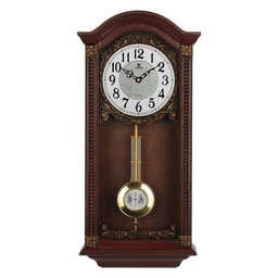 This is a wooden wall-mounted pendulum clock with a classic, antique-style cabinet. It appears designed for a home or living room audience (unisex), featuring a carved dark wood case with gold-tone decorative trim, a white analog dial with black numerals, and a brass pendulum visible through an open lower section. Materials suggested by the photo include wood with brass accents; the style is traditional/period-inspired.